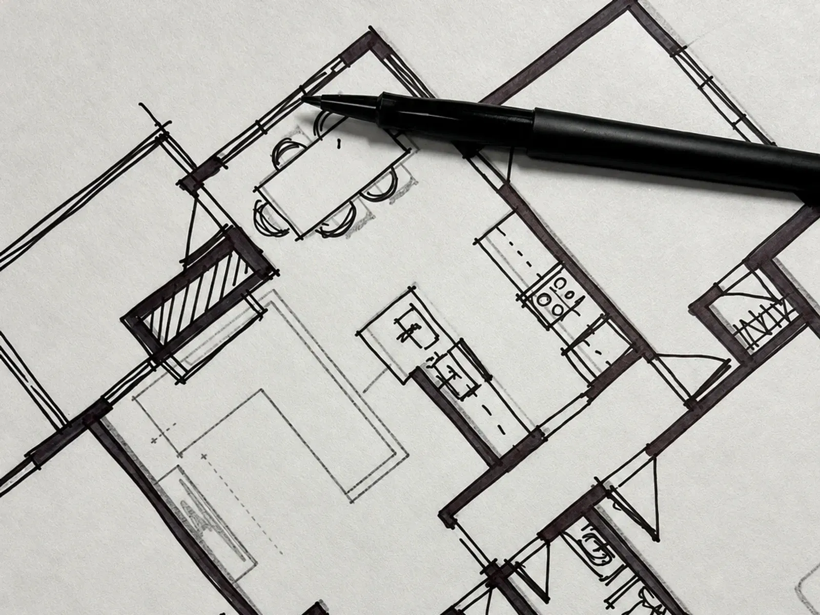 Marker sketch of a floor plan, with a dining area, kitchen, and bathrooms, and a pen resting on the paper